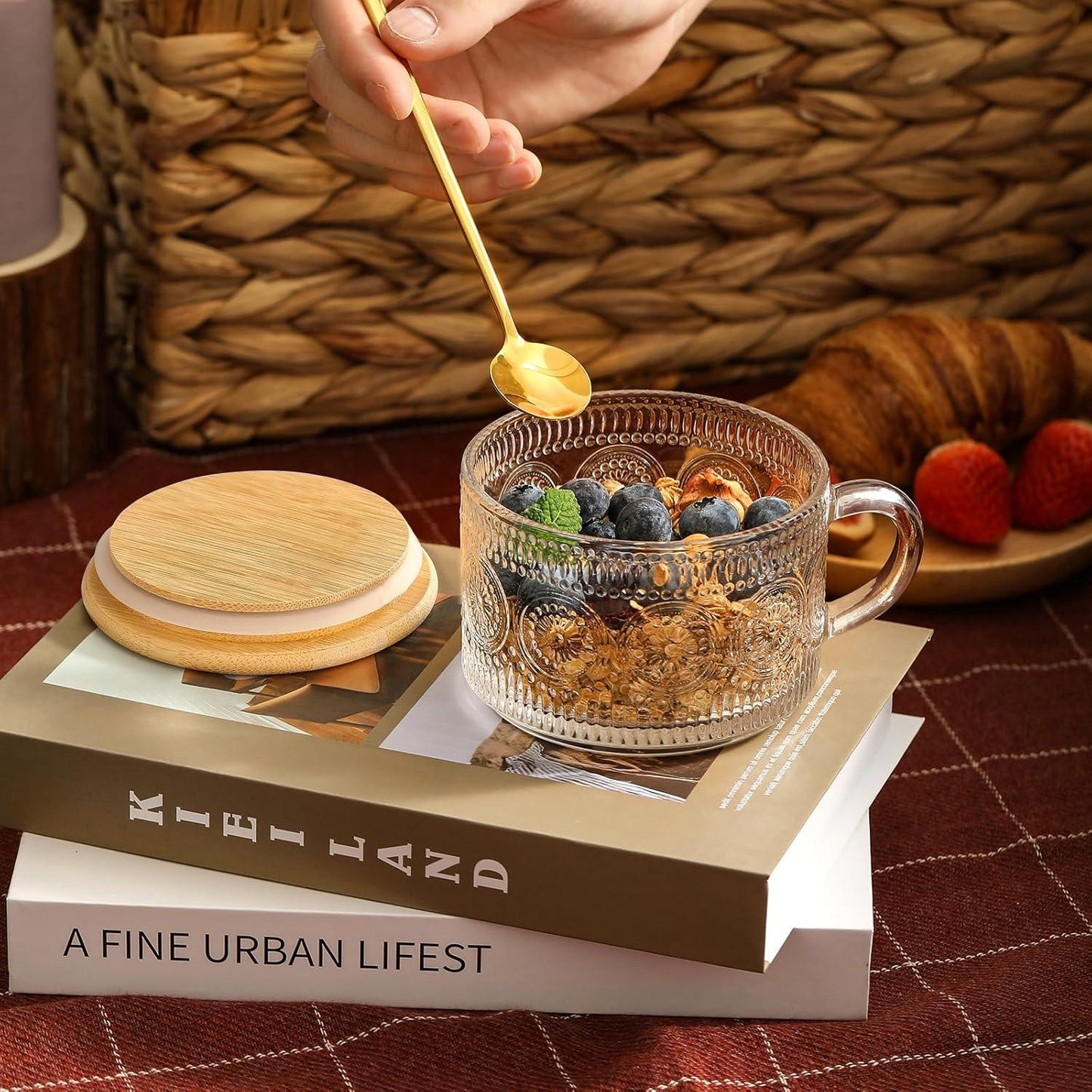 Vintage embossed glass coffee mug with bamboo lid and golden spoon, filled with granola and blueberries on books