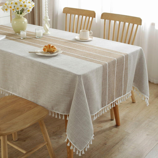 Dining table with a beige and brown striped tablecloth, wooden chairs, and a vase of flowers.